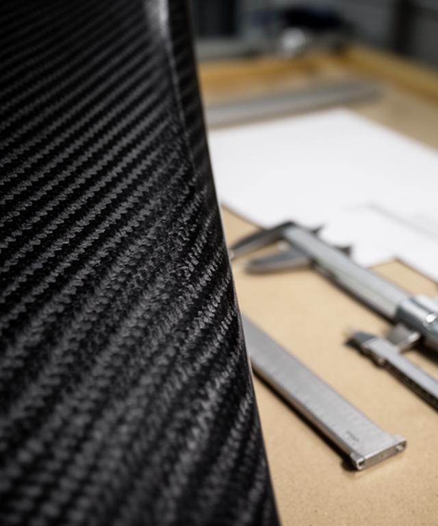 Detalle de fibra de carbono trenzada junto a herramientas de medición sobre una mesa industrial